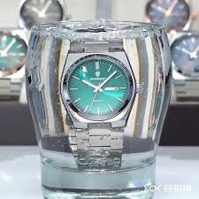 Stainless steel wristwatch submerged in a glass of water with clocks in the background.